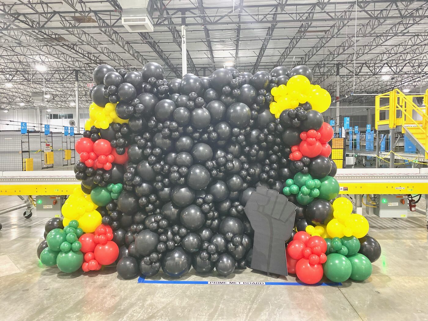 Black balloon wall with red, yellow and green clusters on a warehouse floor