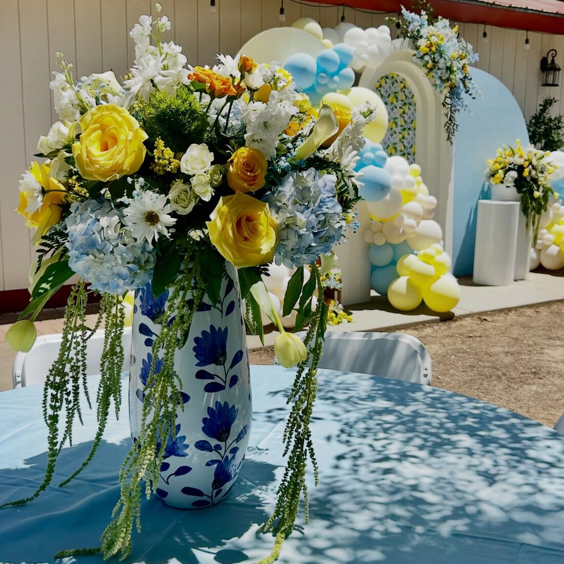 Yellow roses and blue hydrangeas in a painted vase in front of a pastel arch
